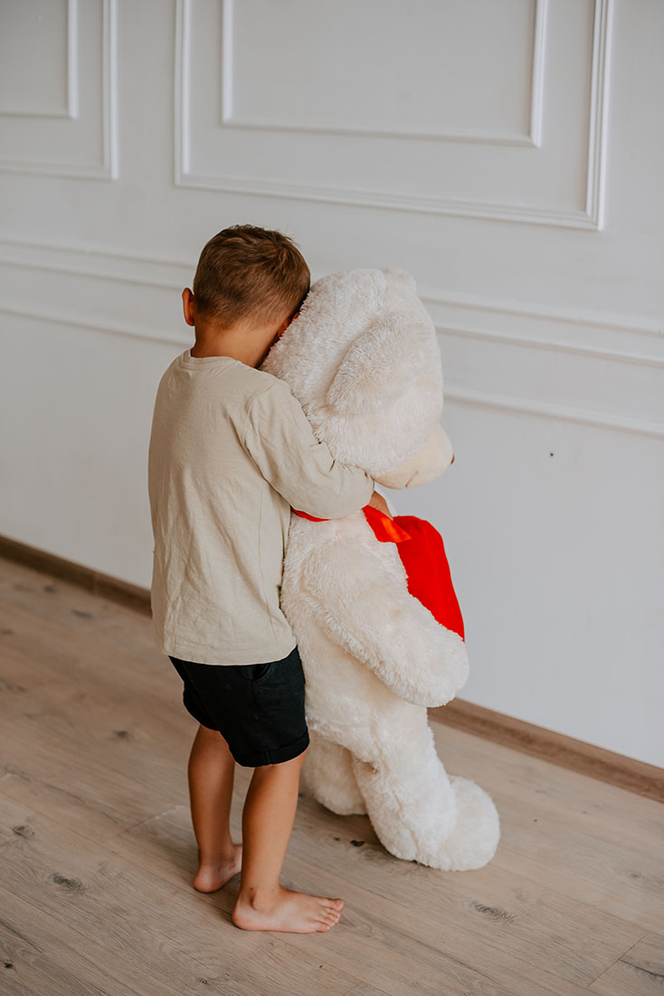 child with autism holding a stuffed bear facing a wall