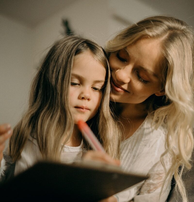 mother helping daughter with autism write on a page