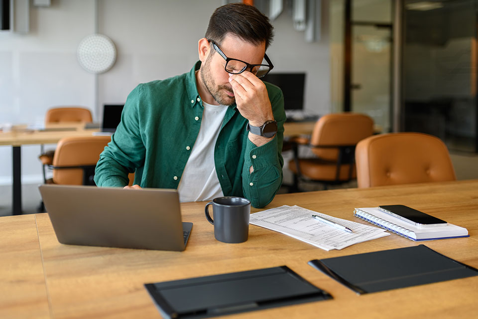 Exhausted male manager rubbing eyes in stress while working over project on laptop at his workplace