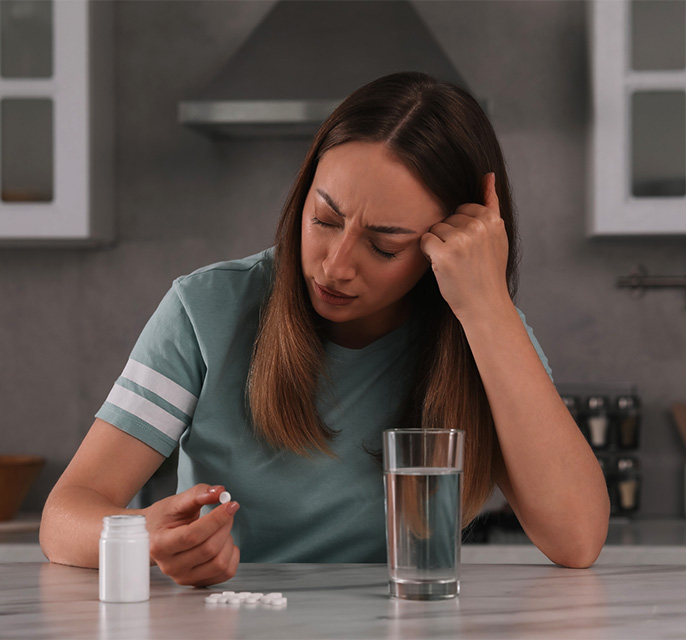 Depressed woman with glass of water and antidepressant pills at table in kitchen